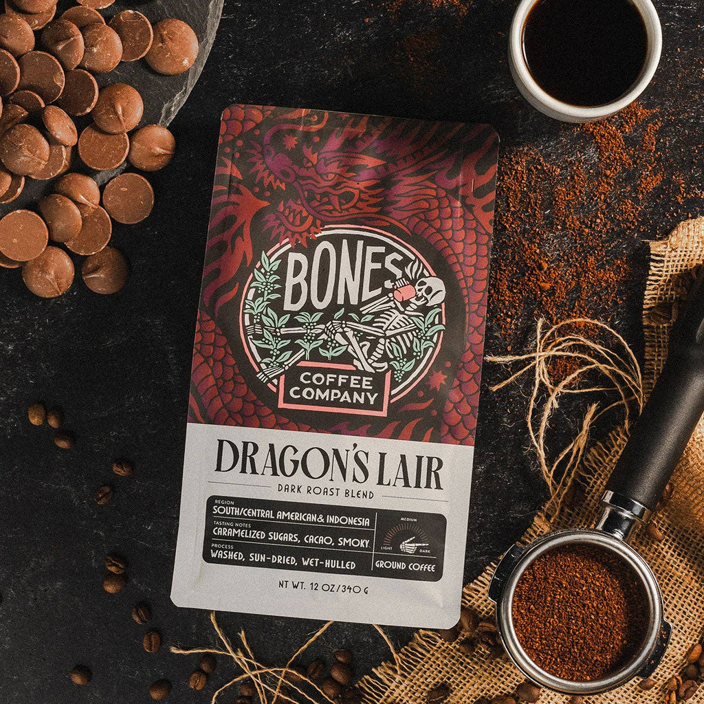 Bones Coffee Company Dragon's Lair coffee package with coffee beans and a cup on a dark surface