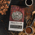 Bones Coffee Company Dragon's Lair coffee package with coffee beans and a cup on a dark surface