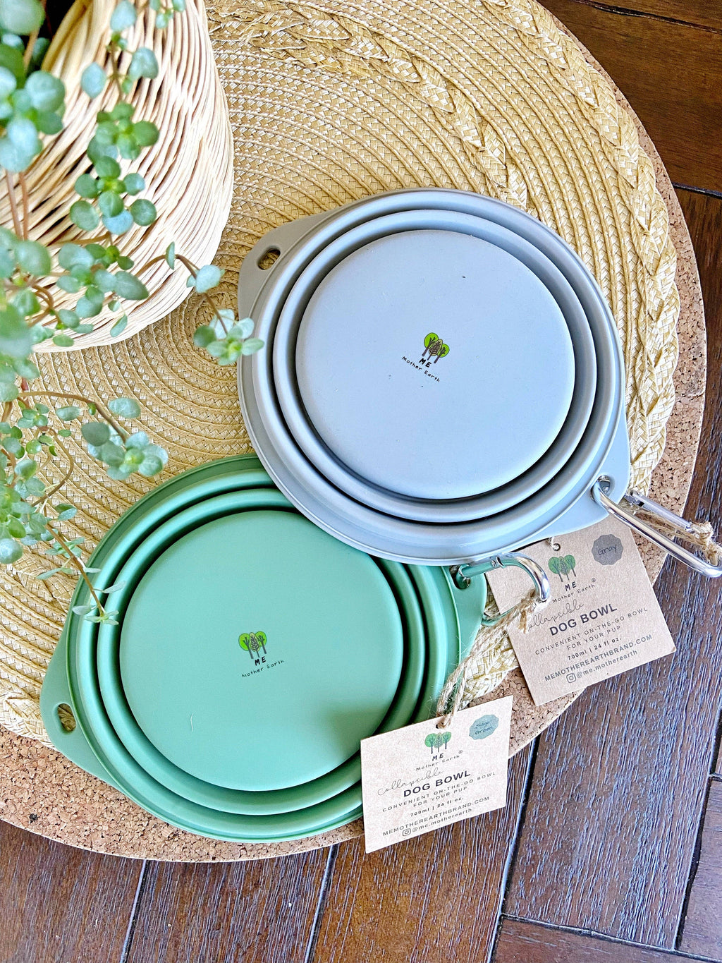 Set of collapsible bowls in green and blue on a woven mat with a plant and business card in the background.