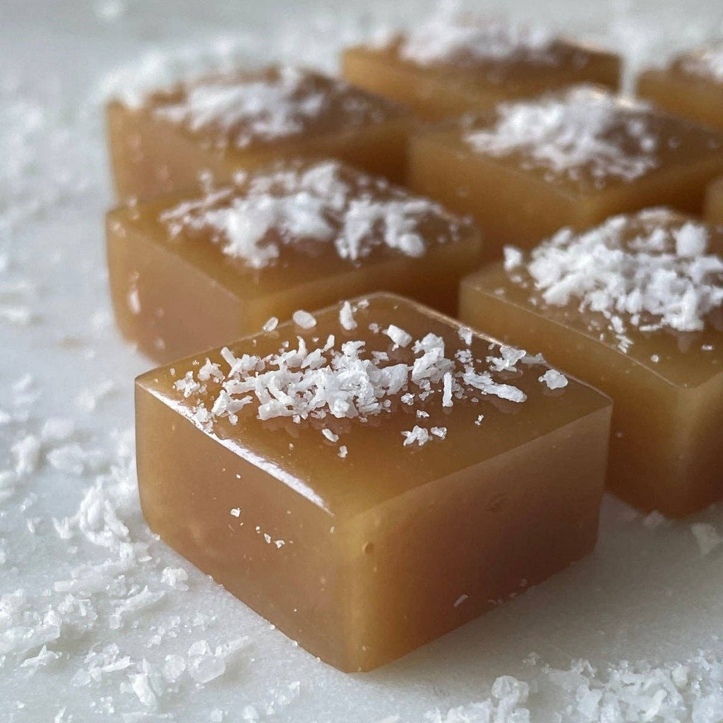 Square pieces of caramel candy with coconut flakes on a white surface