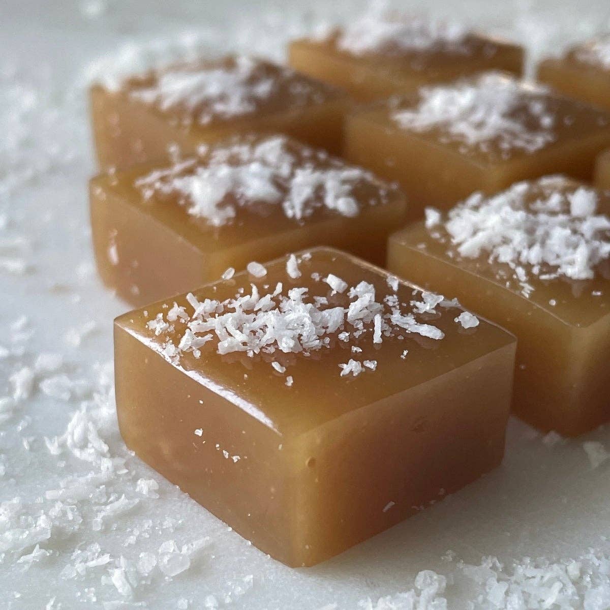Square pieces of caramel candy with coconut flakes on a white surface