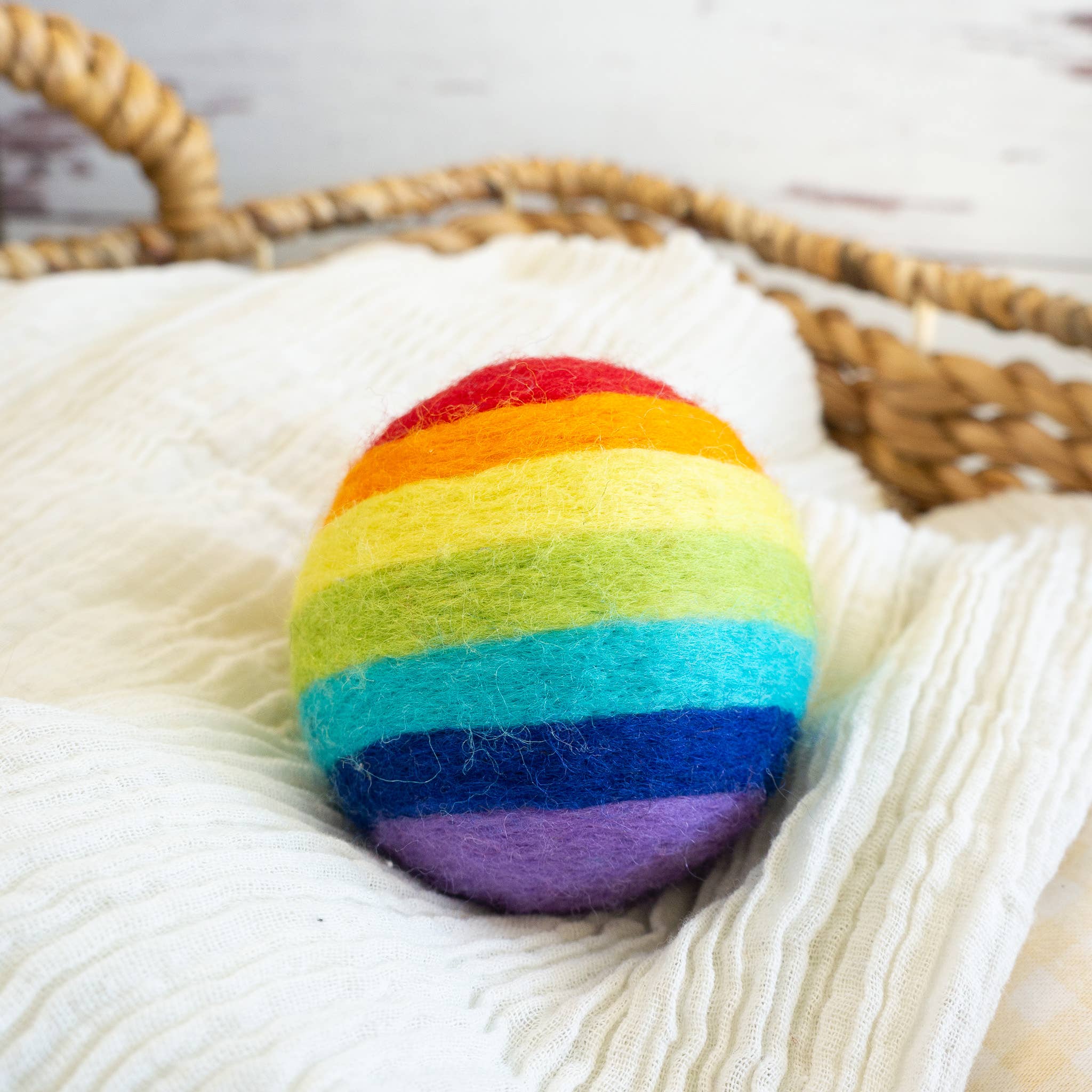 Colorful a rainbow-colored wool dryer ball on a textured surface with a woven basket in the background.