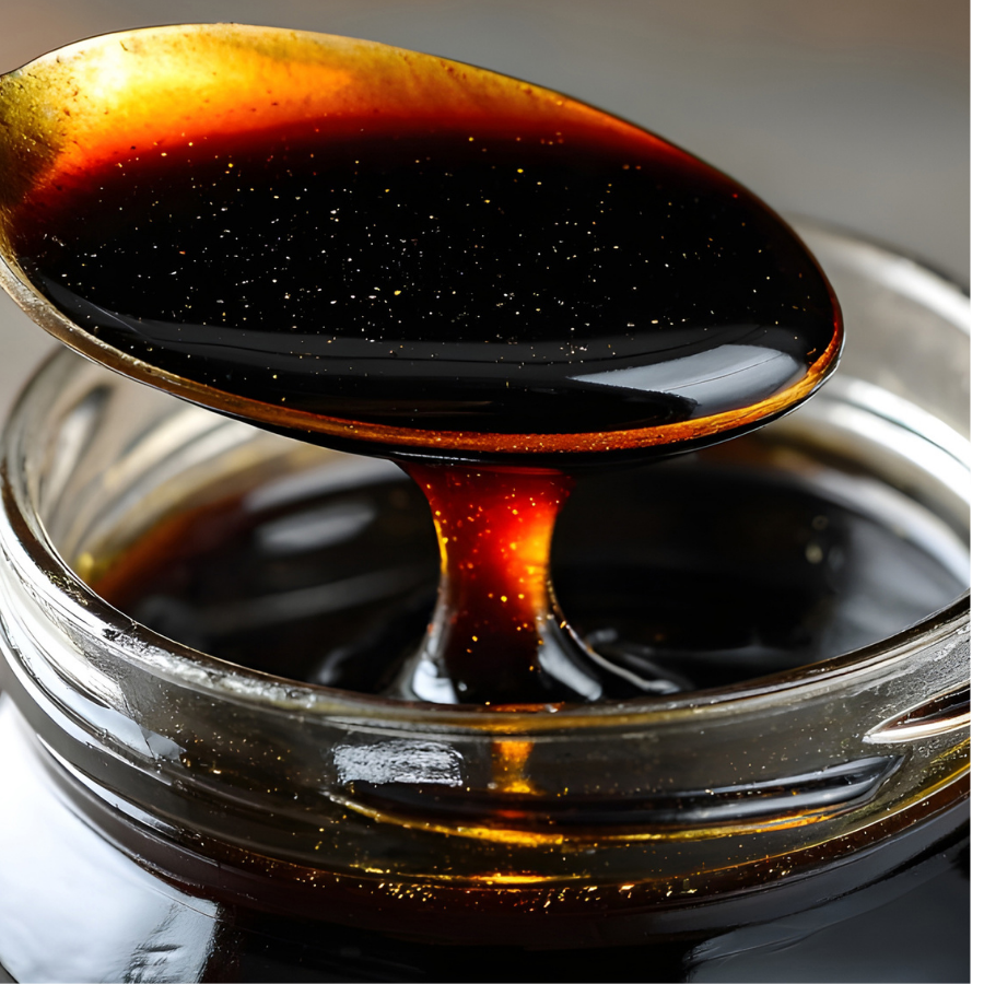 Spoonful of dark maple syrup being lifted from a glass container 