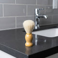 Shaving brush on a bathroom counter with a sink and faucet in the background