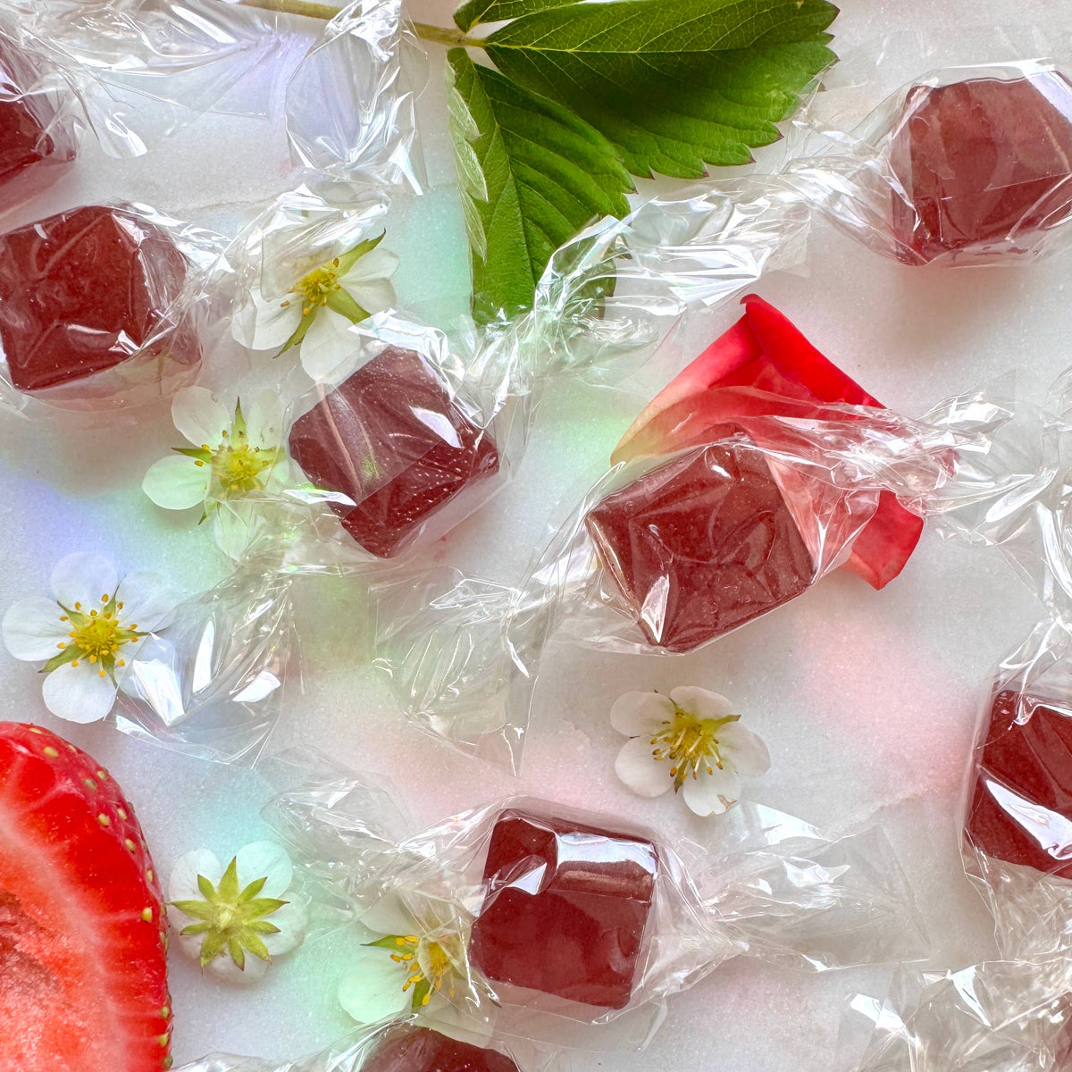 Red jelly cubes in clear wrappers on a white background with flowers and leaves.