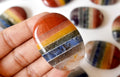 Close-up of a hand holding a rainbow-colored stone with blurred stones in the background.