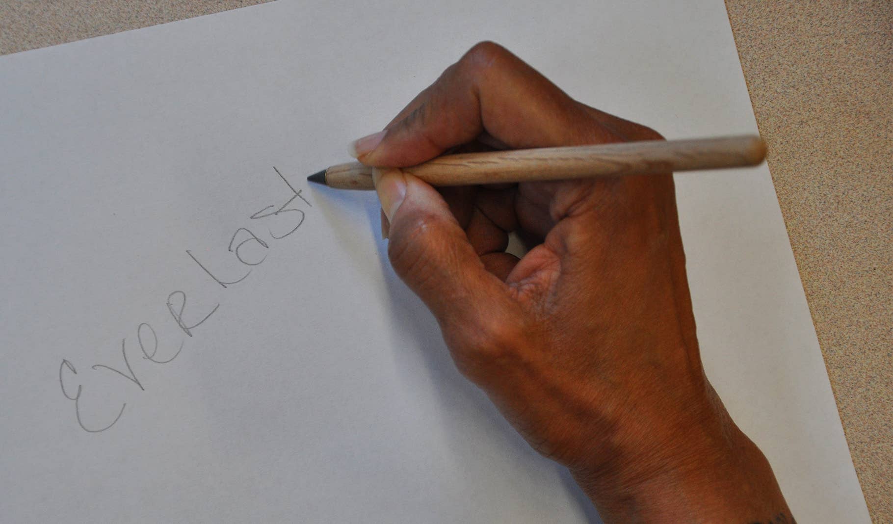 Hand writing 'Everlast' with an everlasting pencil on white paper.