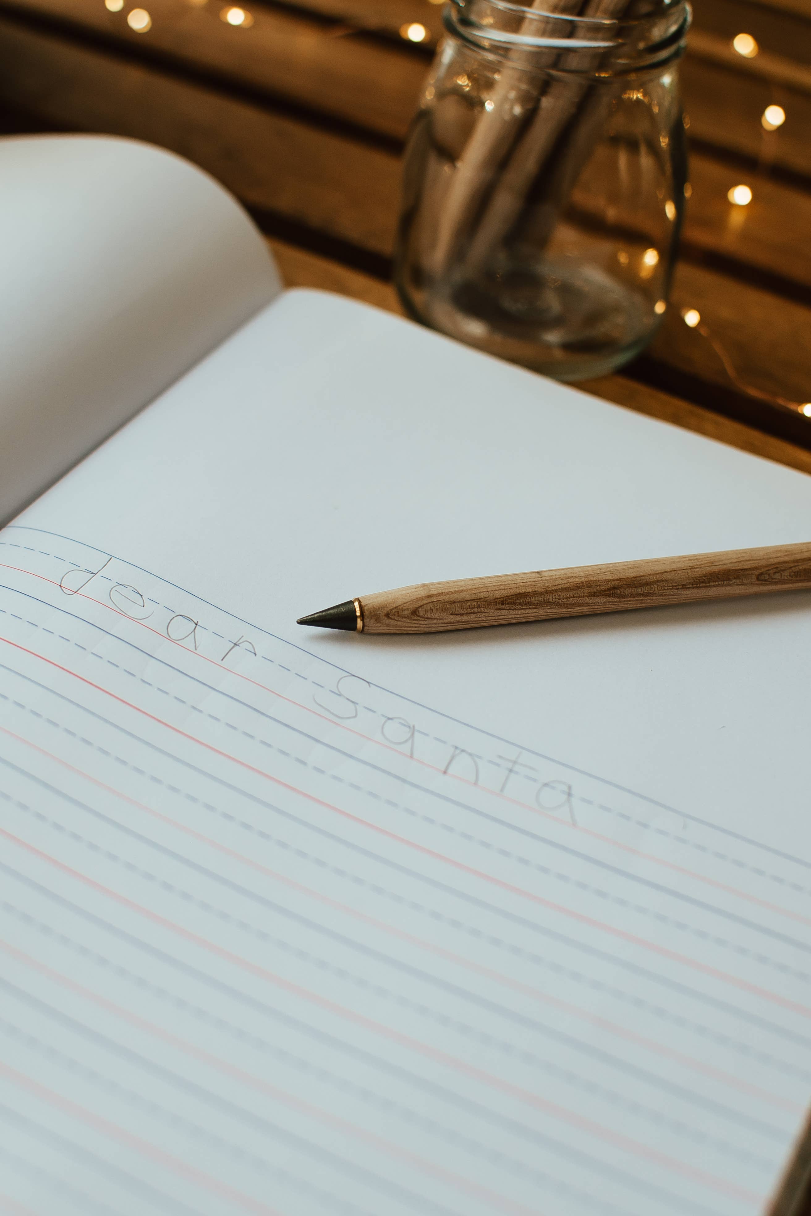 Notebook with a pencil on a wooden surface with fairy lights