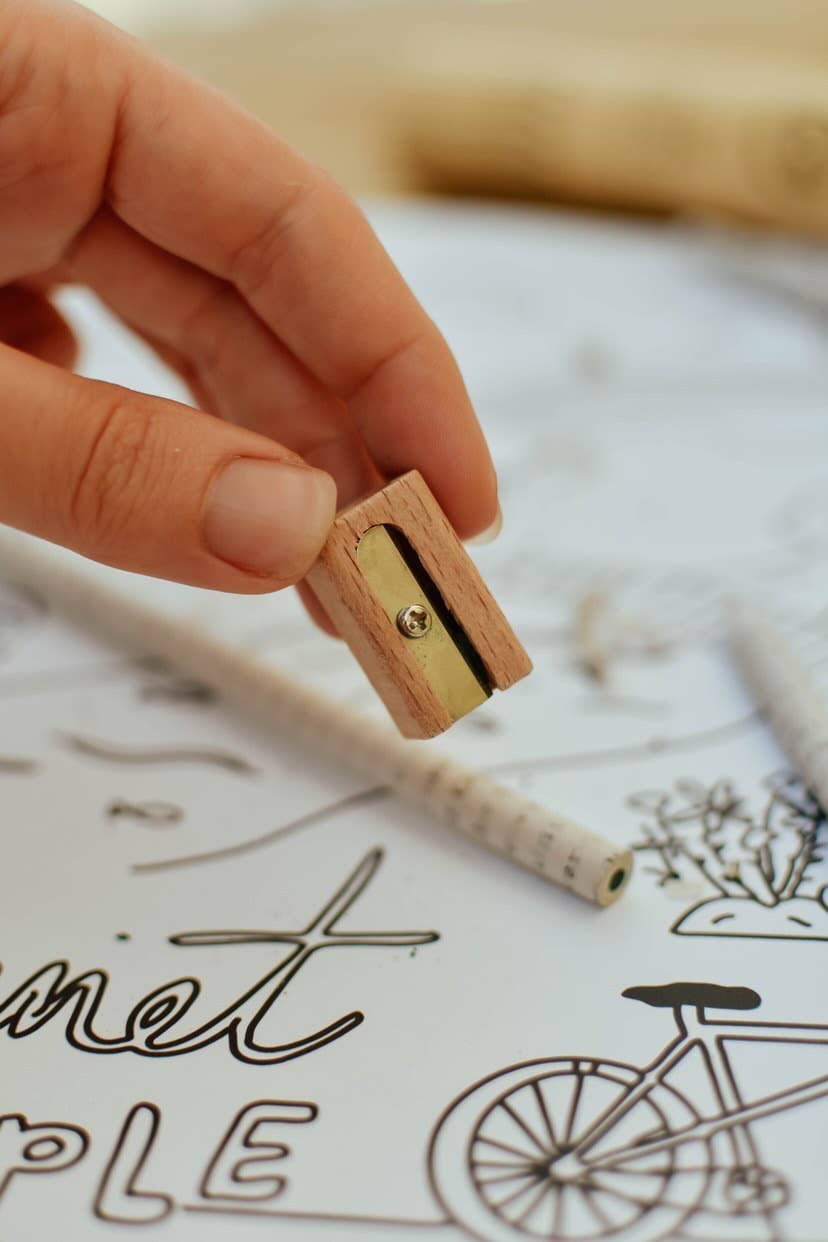 Hand holding a small wooden pencil sharpener with a blurred background of a coloring book page.