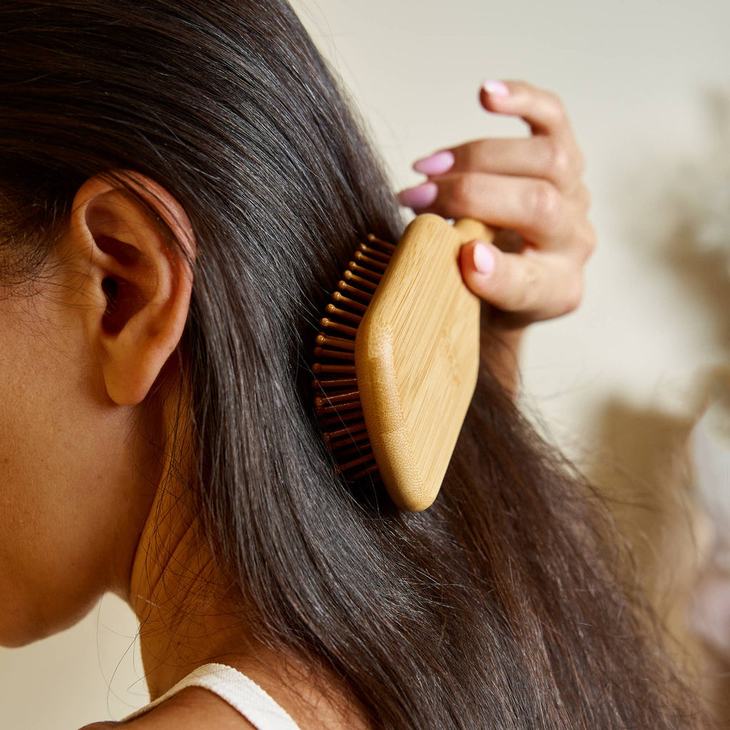 Person brushing their hair with a wooden brush against a neutral background