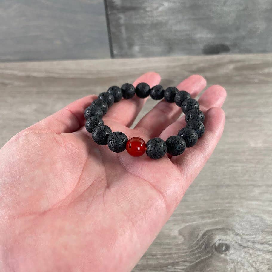 Black beaded bracelet with a red stone held in a hand on a wooden surface