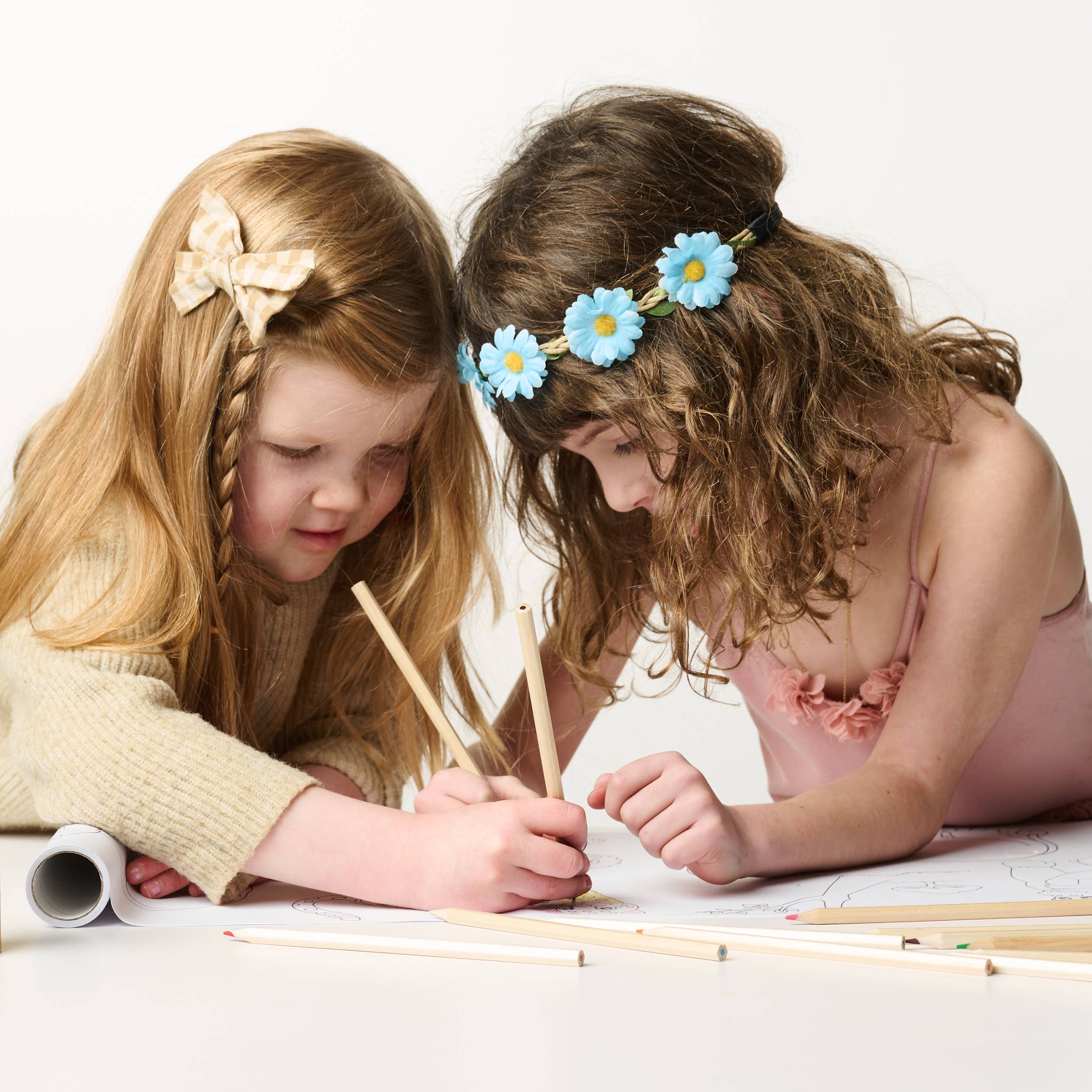 Two young girls drawing with colored pencils on a white surface.