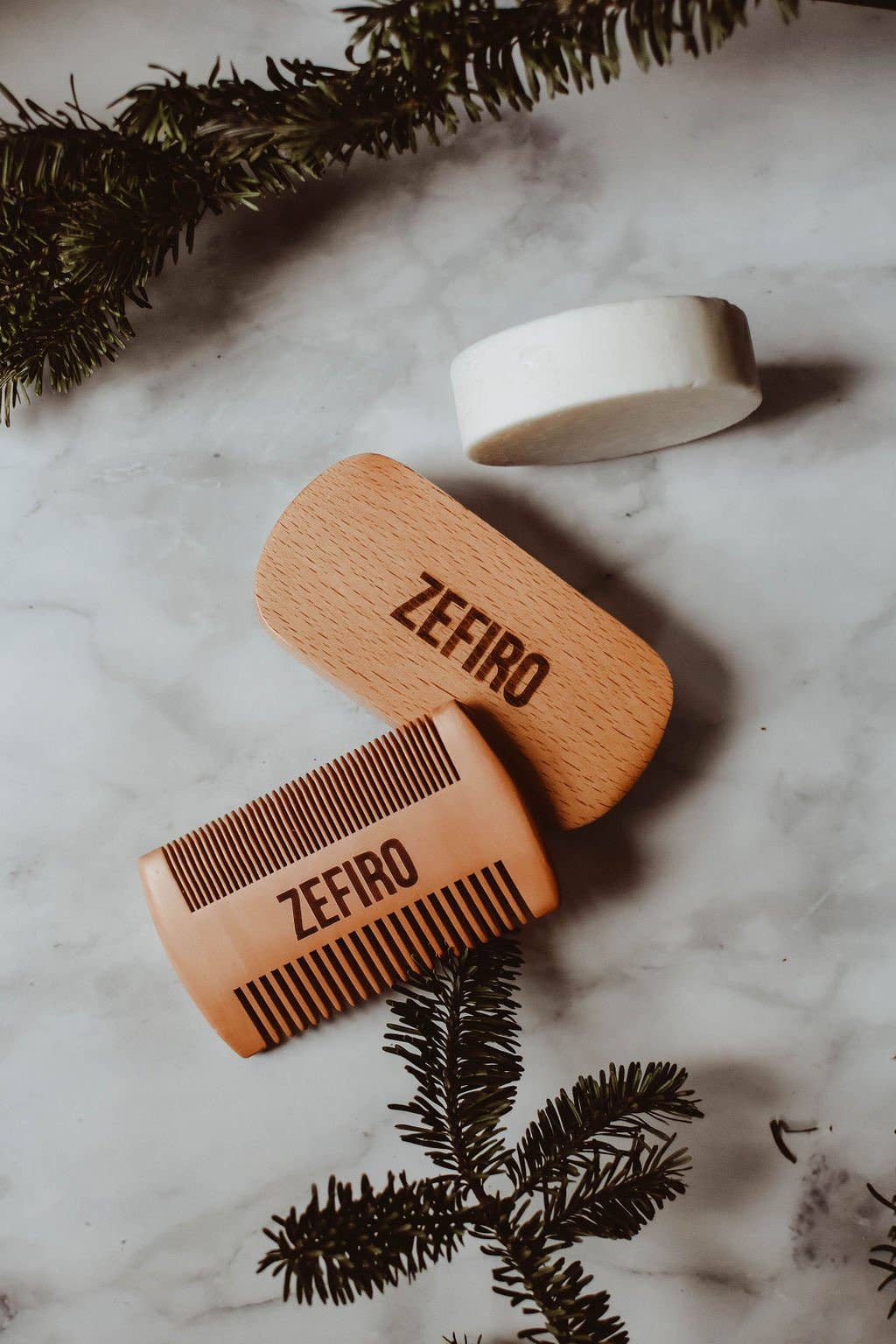 Wooden comb and soap with 'Zefiro' branding on a marble surface with greenery.