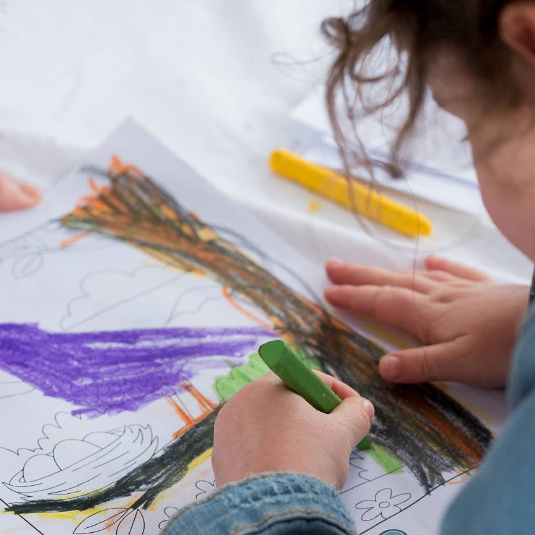 Child coloring a picture with crayons on a white sheet of paper