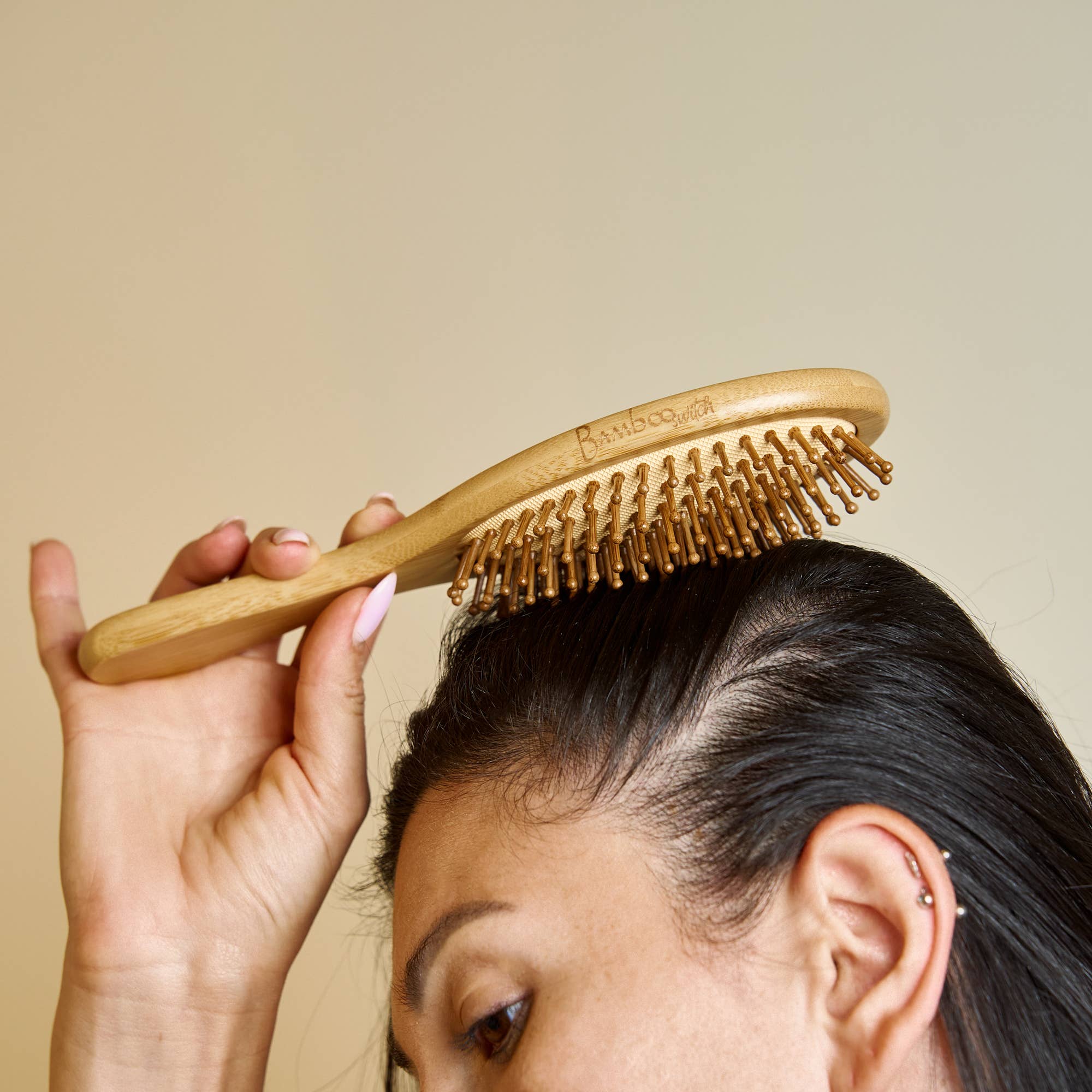 Person using a wooden hairbrush on their head against a beige background