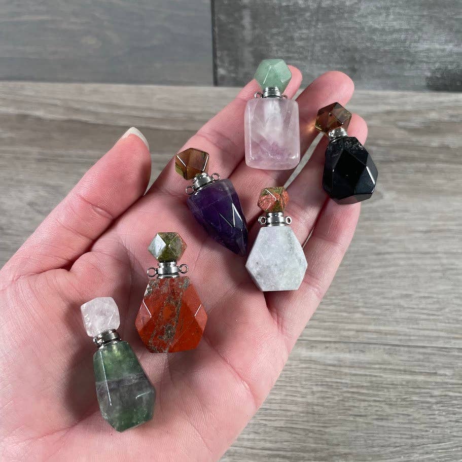 Hand holding small crystal bottles with various colored tops on a wooden surface