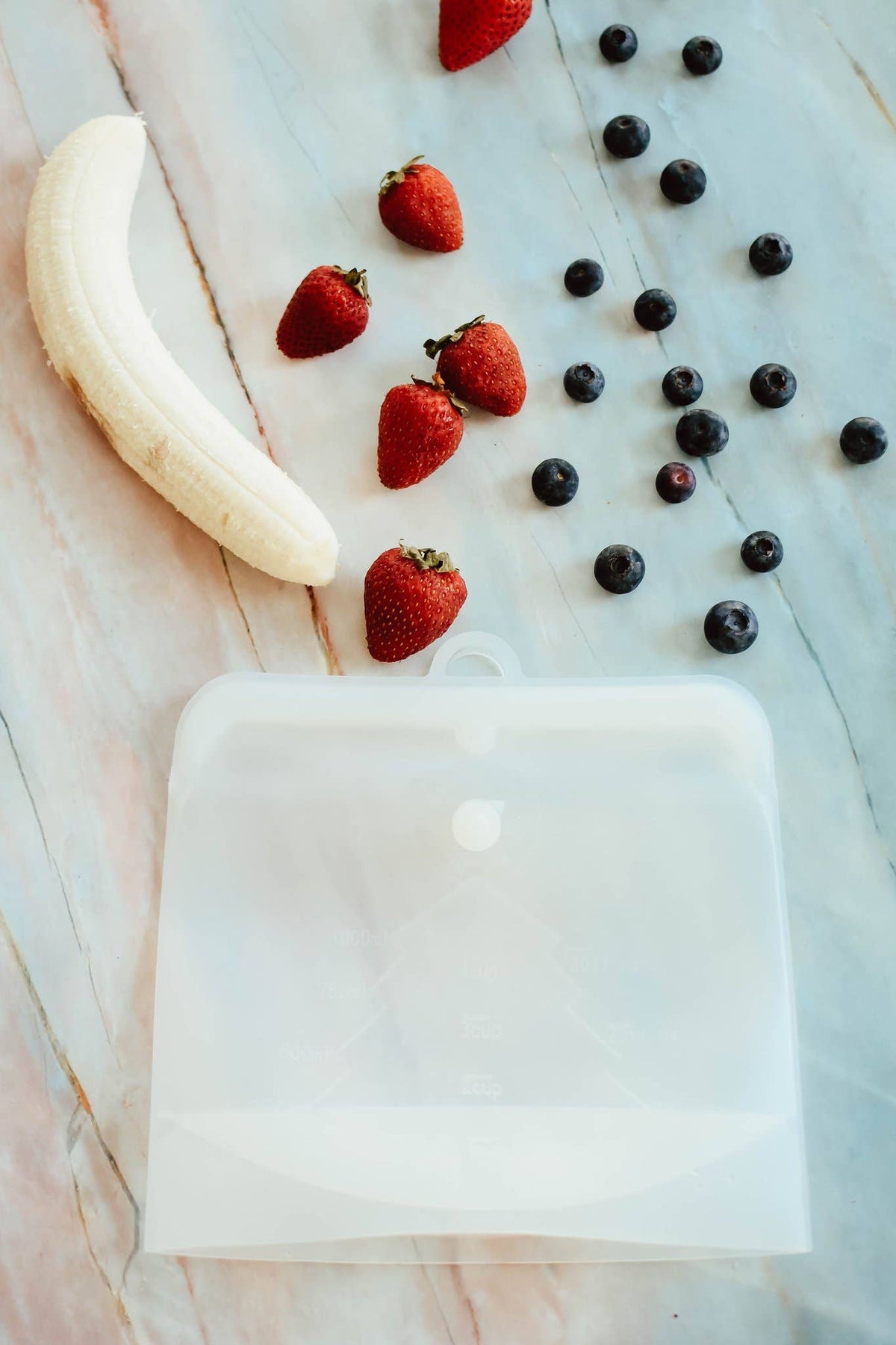 Fruit including strawberries, blueberries, and a banana on a marble surface.