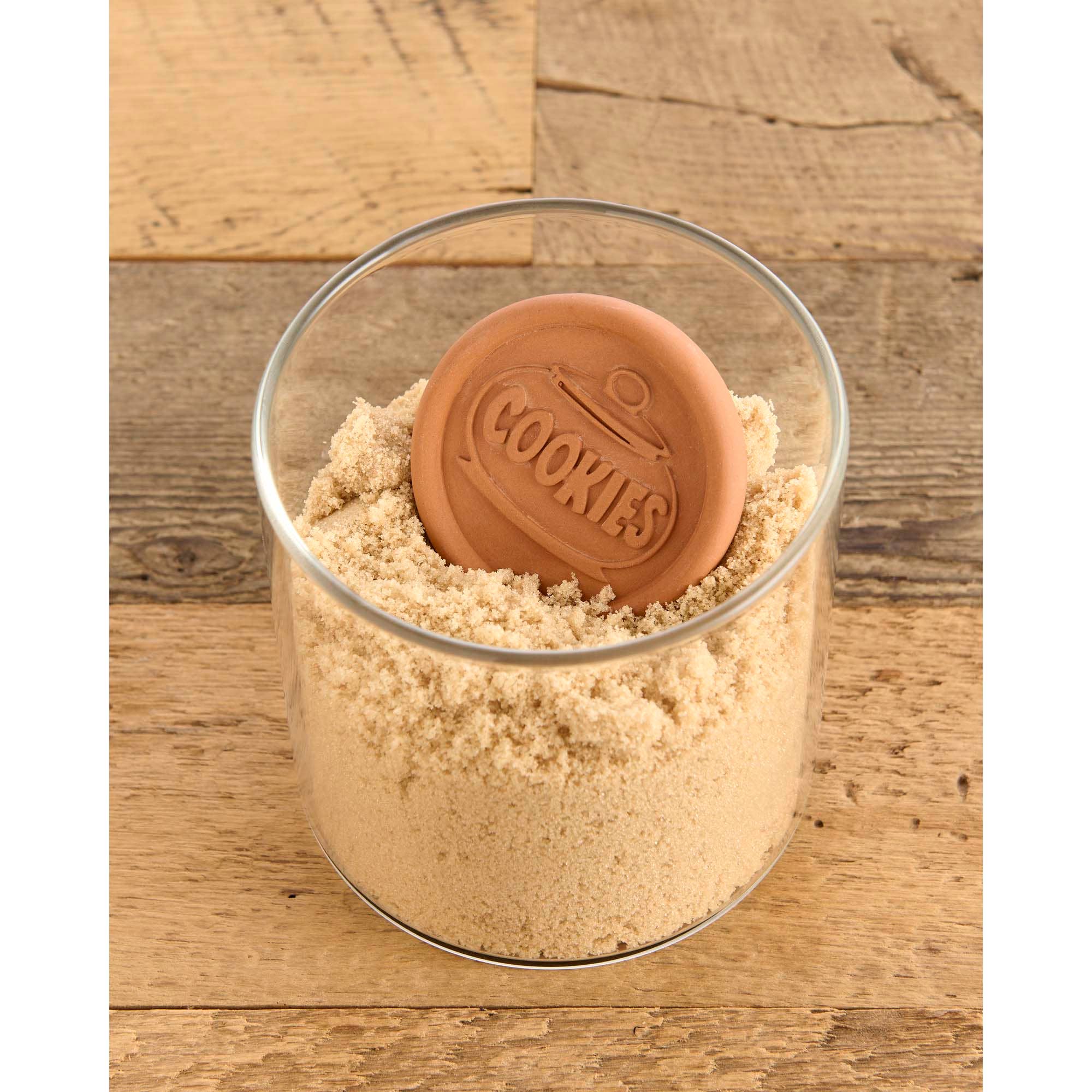 Glass container filled with a brown substance and a 'COOKIES' branded cookie on a wooden surface
