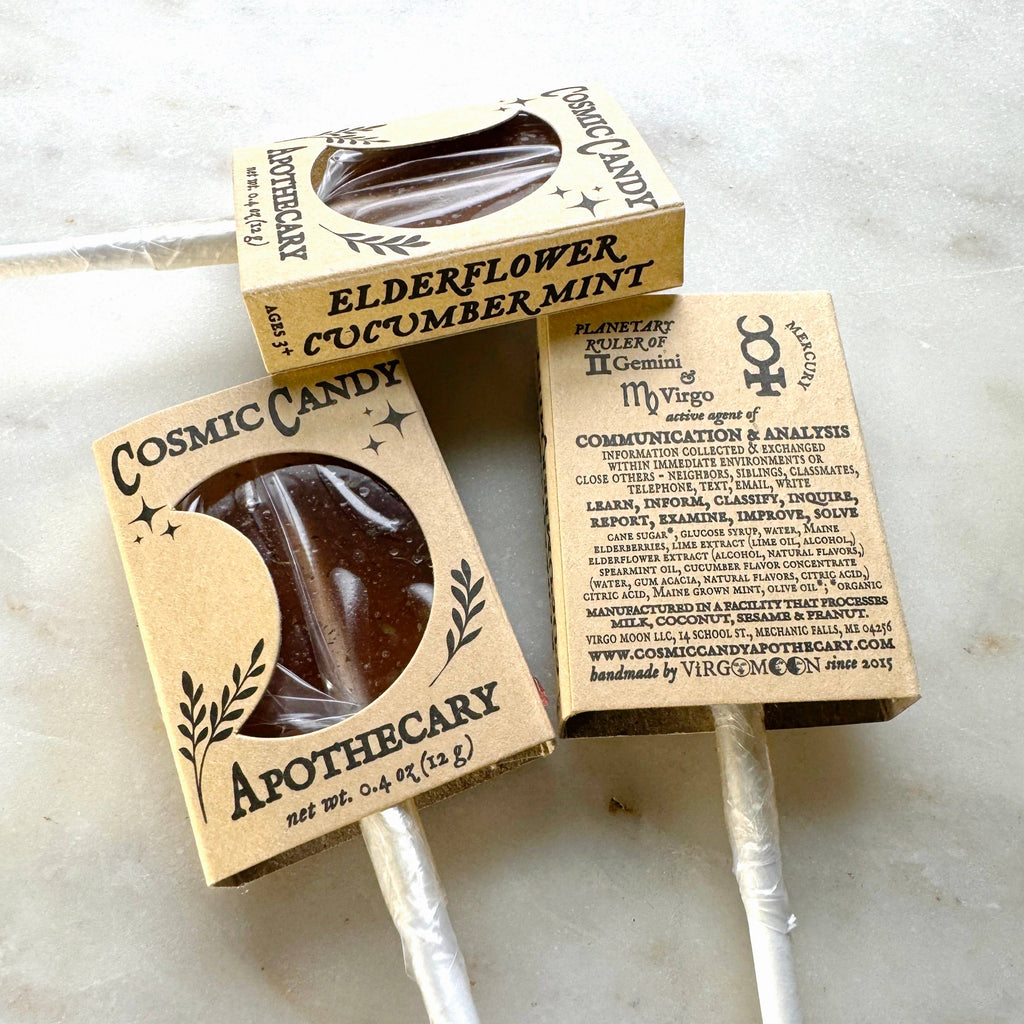 Two Cosmic Candy Apothecary lollipops in cardboard packaging on a marble surface.