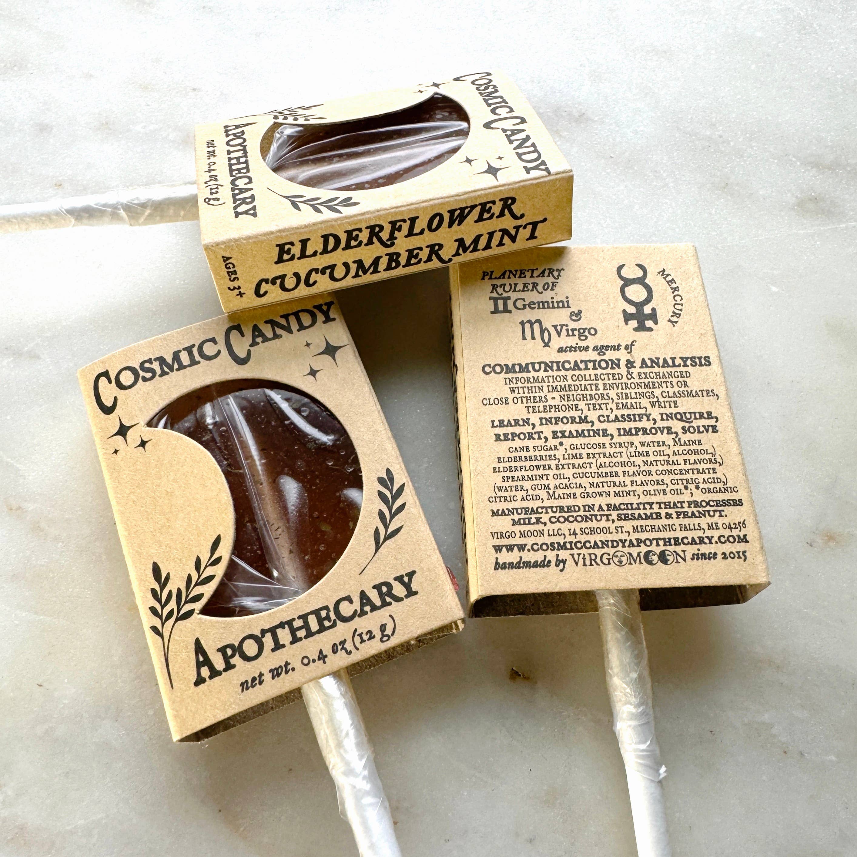 Two Cosmic Candy Apothecary lollipops in cardboard packaging on a marble surface.