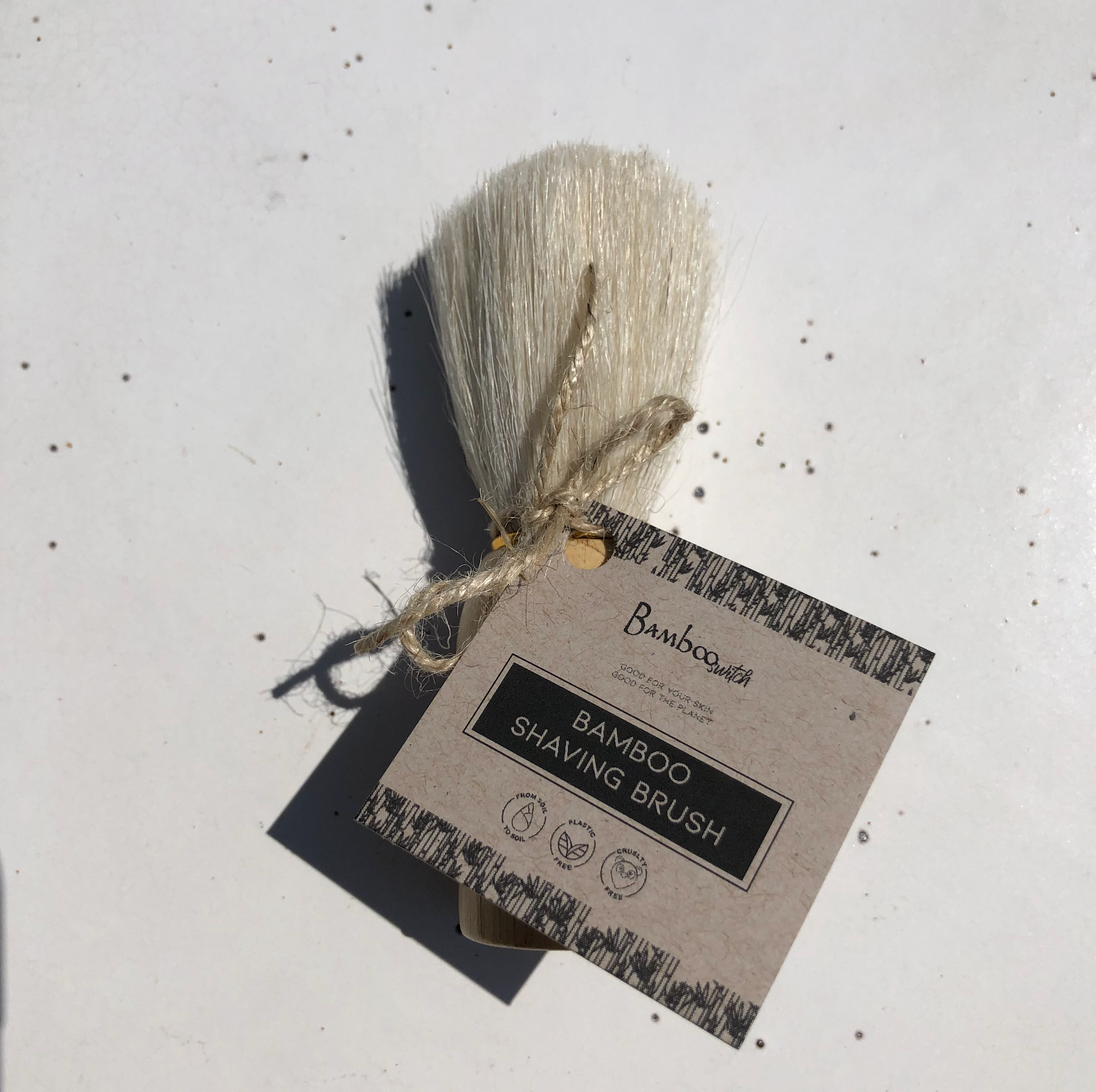 Bamboo shaving brush with packaging on a textured white background
