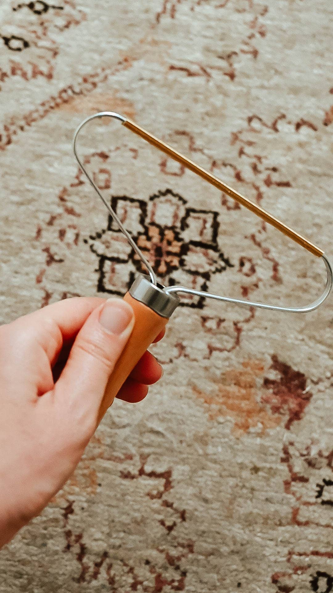 Hand holding a metal lint remover over a patterned rug