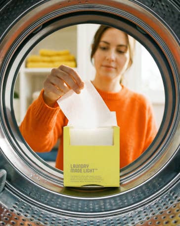 Woman holding a yellow box labeled 'Laundry Made Easy' inside a washing machine.