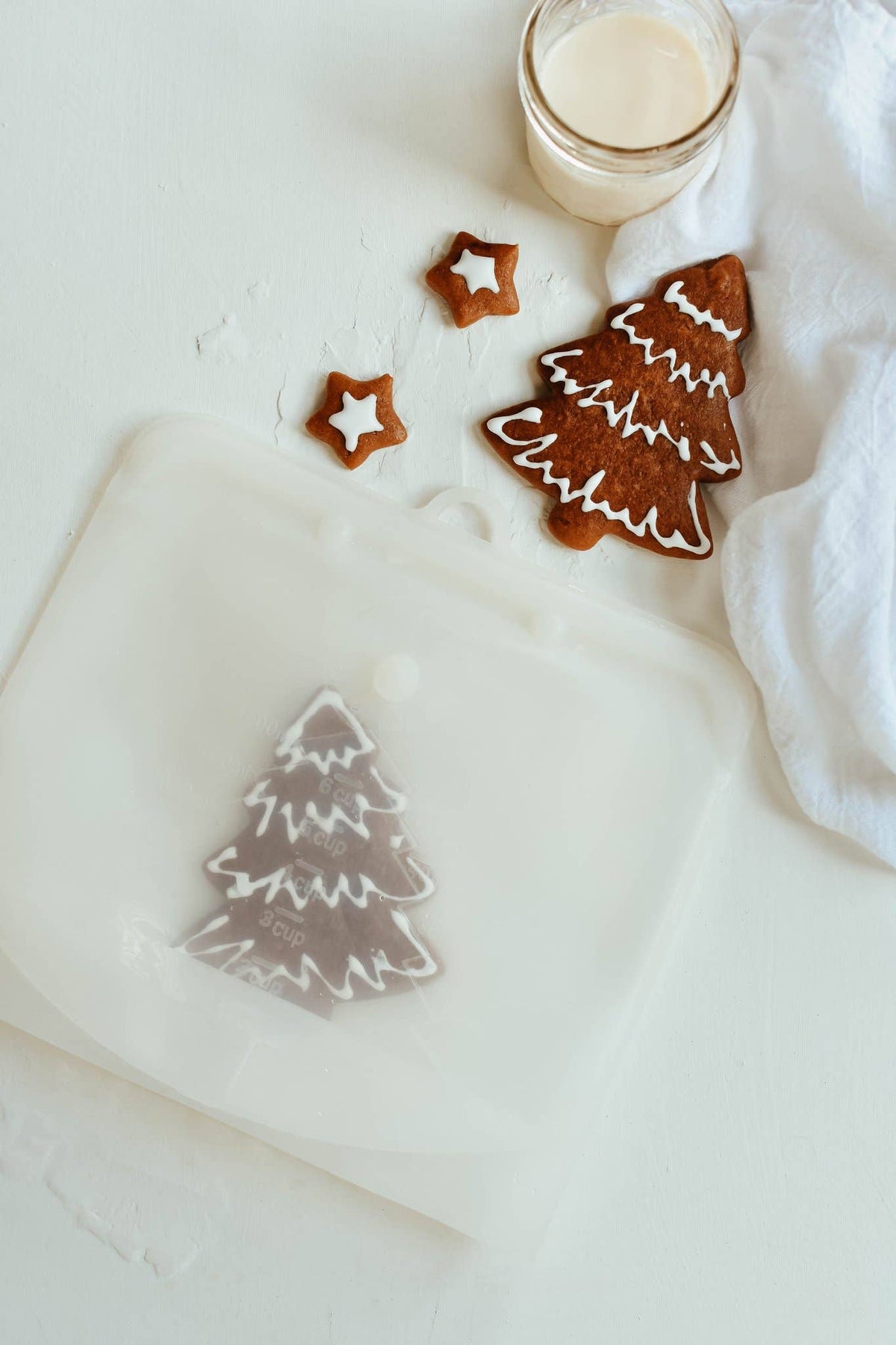 Christmas cookies shaped like trees and stars on a white surface with a glass of milk.