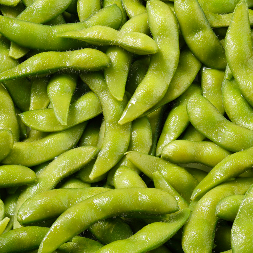 A close-up, top-down view of a pile of fresh, glossy green edamame soybeans in their pods.