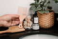Hand holding a wooden pick with a plant and bottles in the background