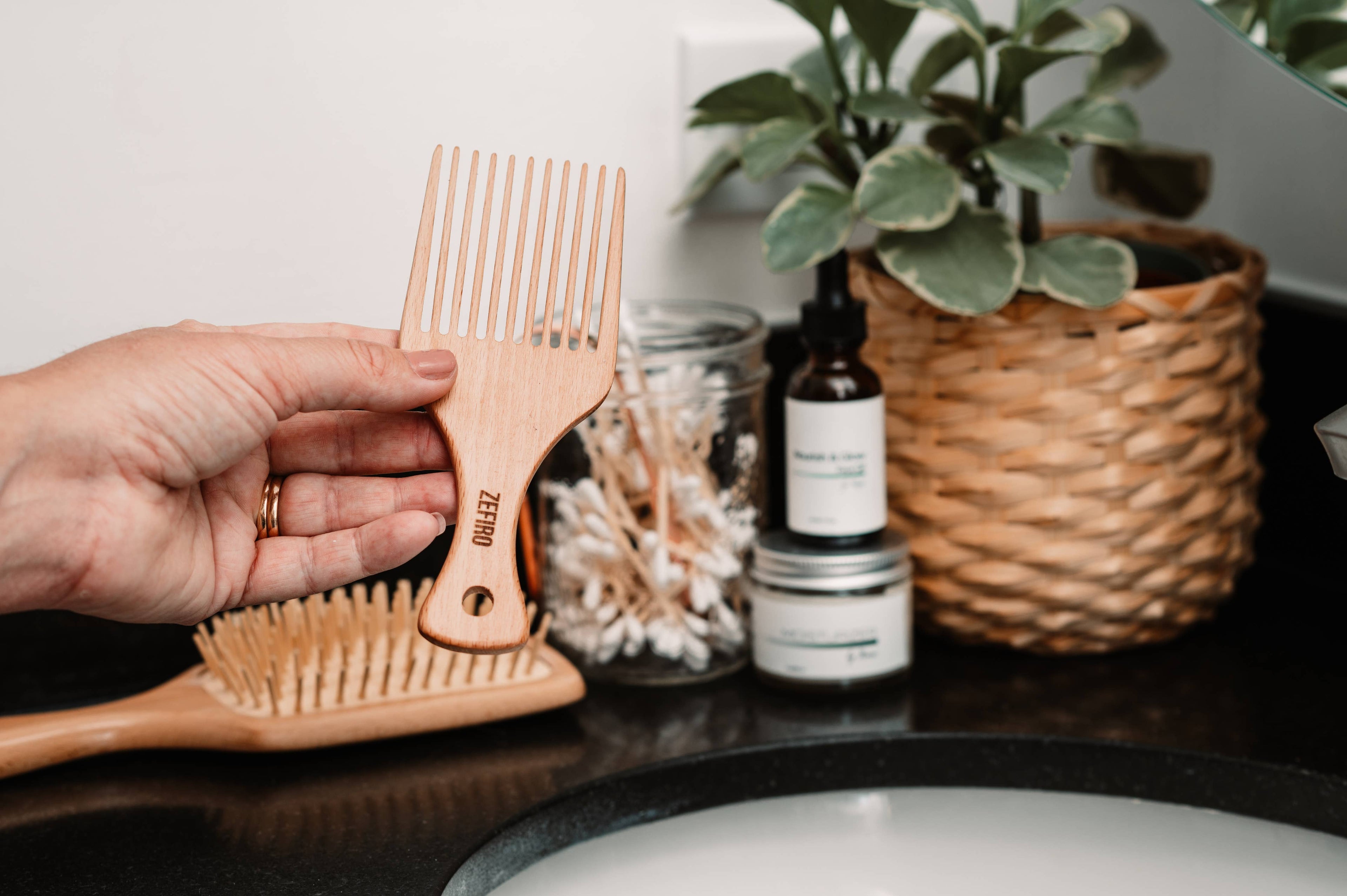 Hand holding a wooden pick with a plant and bottles in the background
