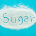 Sugar text written on a pile of sugar crystals against a blue background