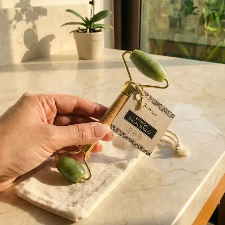 Hand holding a facial roller with a packaging label on a marble surface.