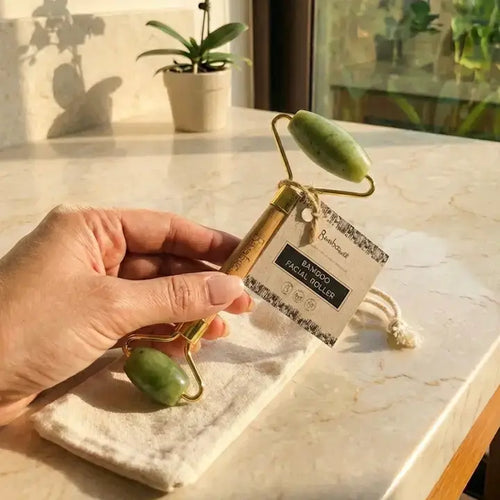 Hand holding a facial roller with a packaging label on a marble surface.