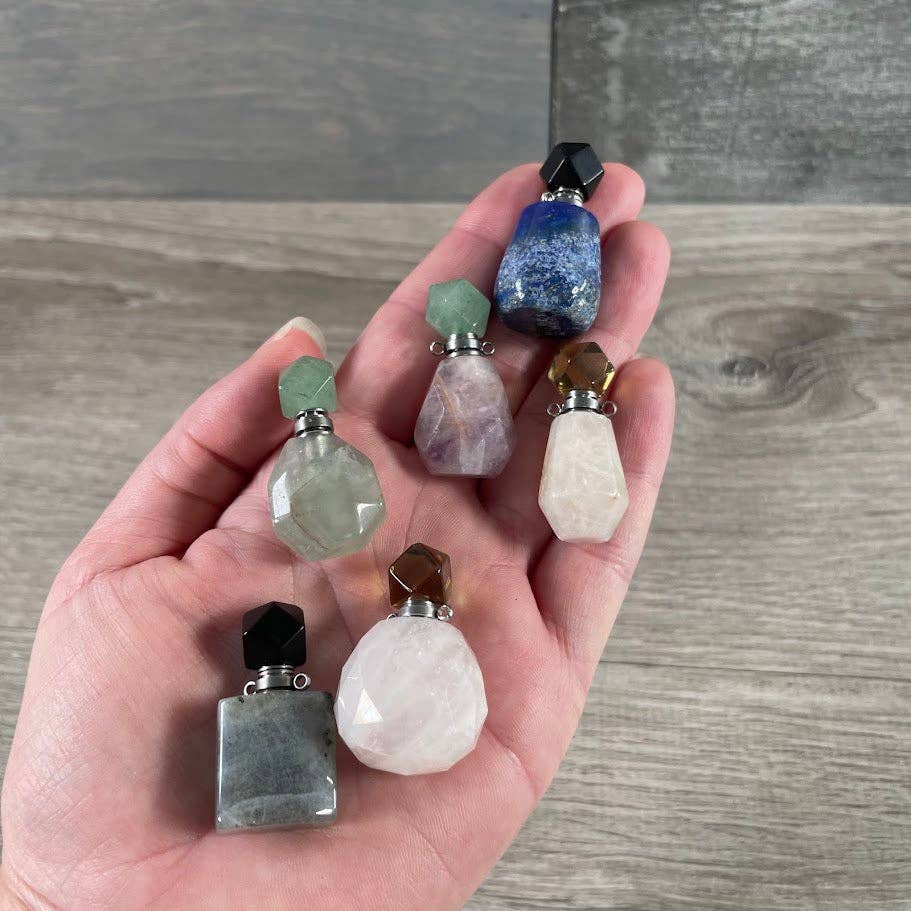 Hand holding a collection of small, faceted stone perfume bottles on a wooden surface.