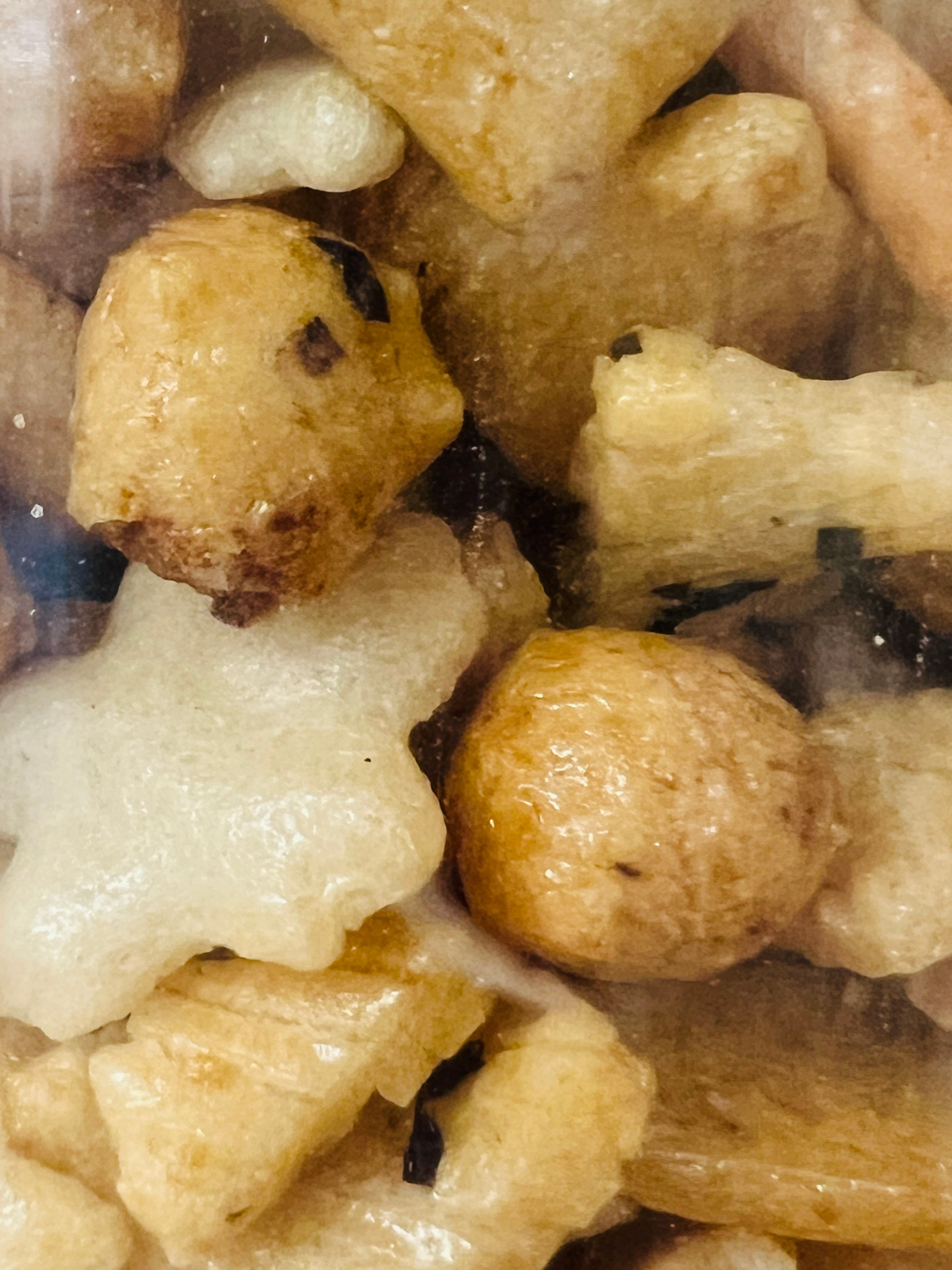Close-up of a mix of white and beige rice crackers shapes of star, balls, squares, and sticks, in a clear container.