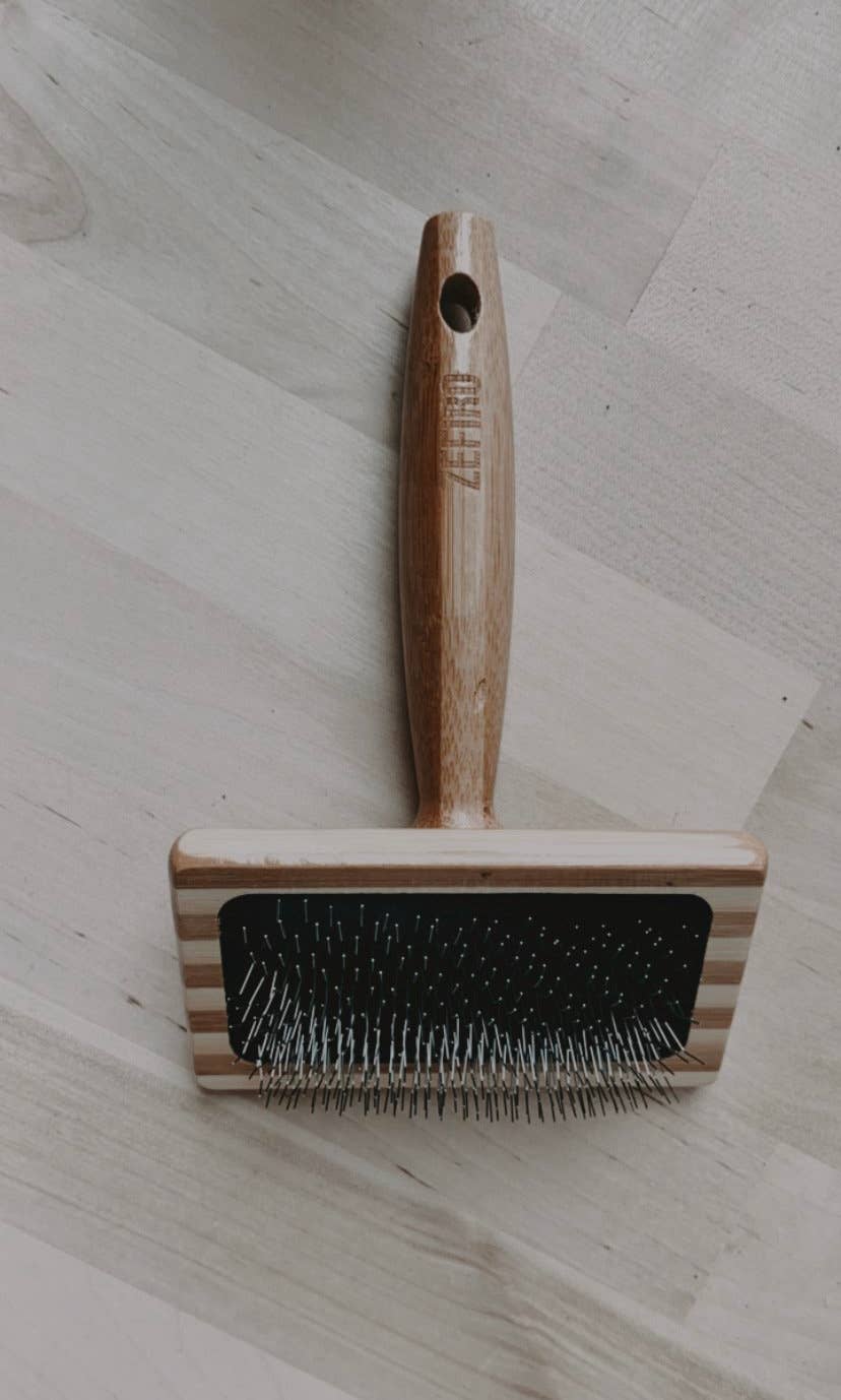 Pet grooming brush with wooden handle on a light wooden surface