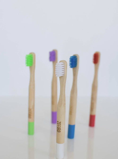 Four bamboo toothbrushes with colored bristles and handles on a white background