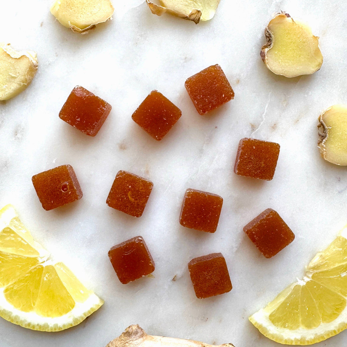 Candy cubes on a marble surface with lemon slices and ginger pieces.
