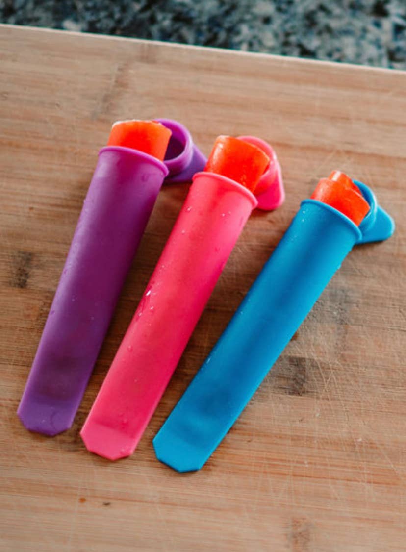 Three colorful popsicle molds on a wooden surface with a stone background.