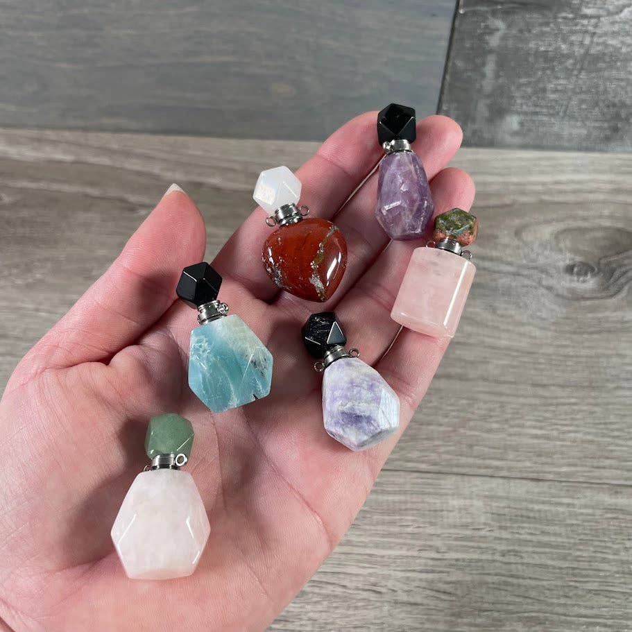 Hand holding various colorful crystal pendants on a wooden surface