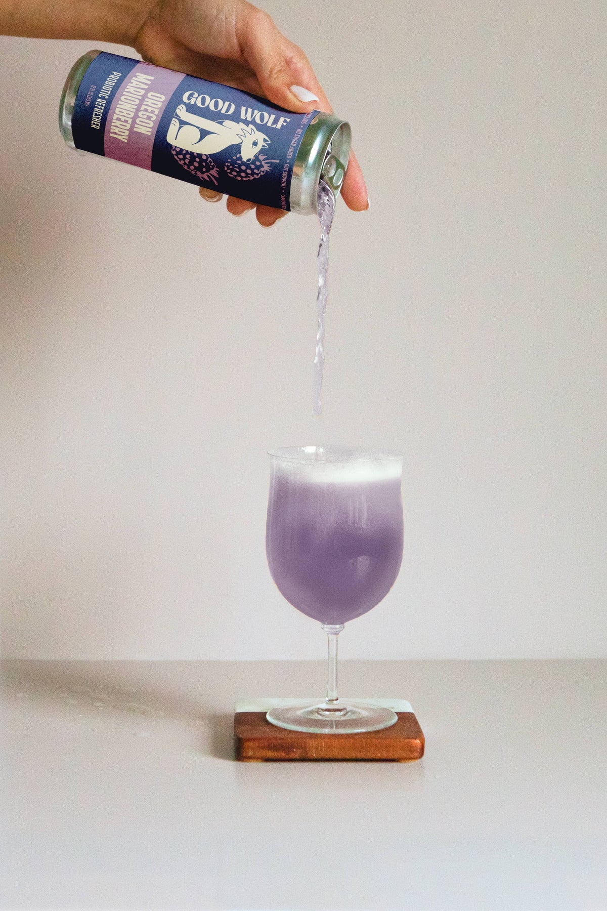 Person pouring a purple beverage from a can labeled 'Good Wolf' into a glass on a white background.