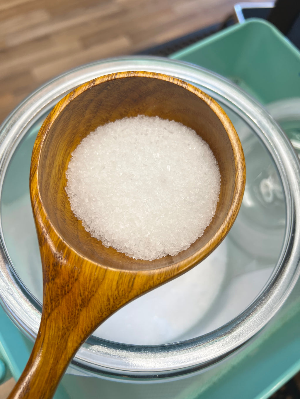 Wooden spoon filled with Epson salts in front of a glass container.