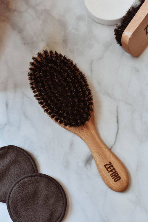 Wooden hairbrush with bristles on a marble surface, branded 'Zefiro'.