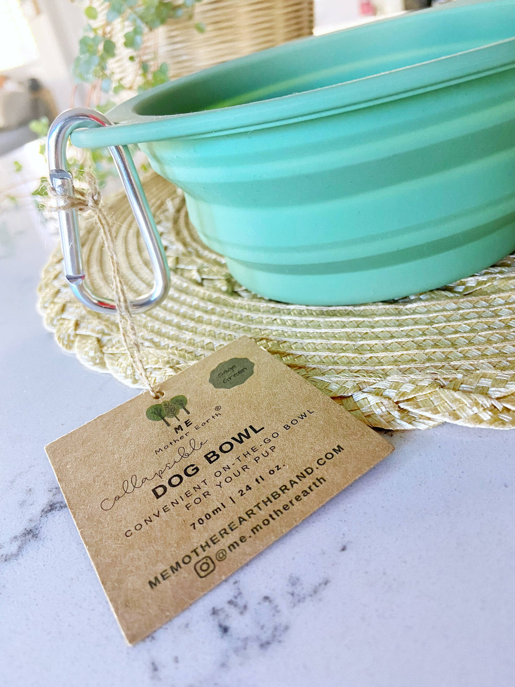 Collapsible turquoise dog bowl with carabiner handle on a marble surface, accompanied by a branded tag.