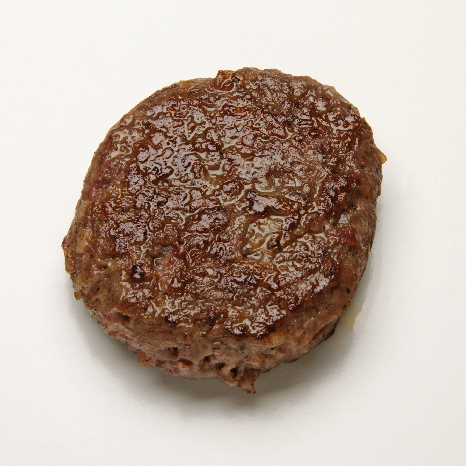 A single cooked vegan sausage patty with a browned, slightly glossy surface, centered on a plain white background.