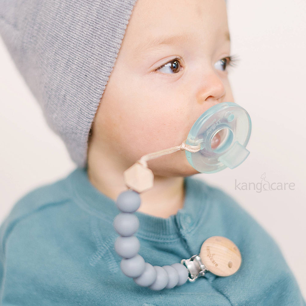 Baby wearing a gray knit hat and blue bib with a teething ring and pacifier holder.