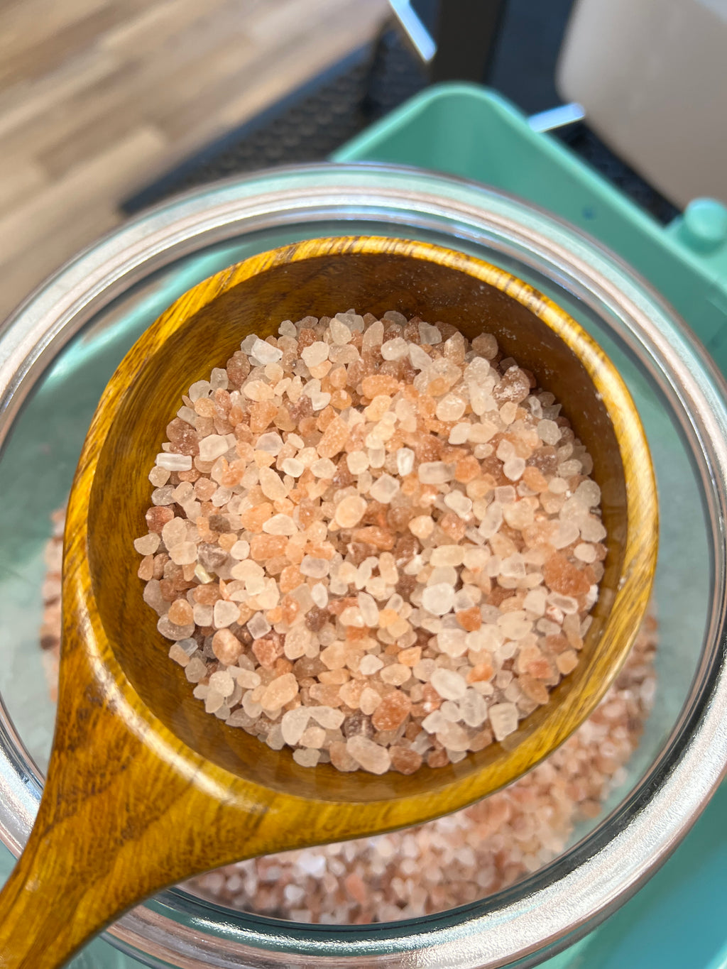 Wooden spoon filled with pink Himalayan salt over a glass container.