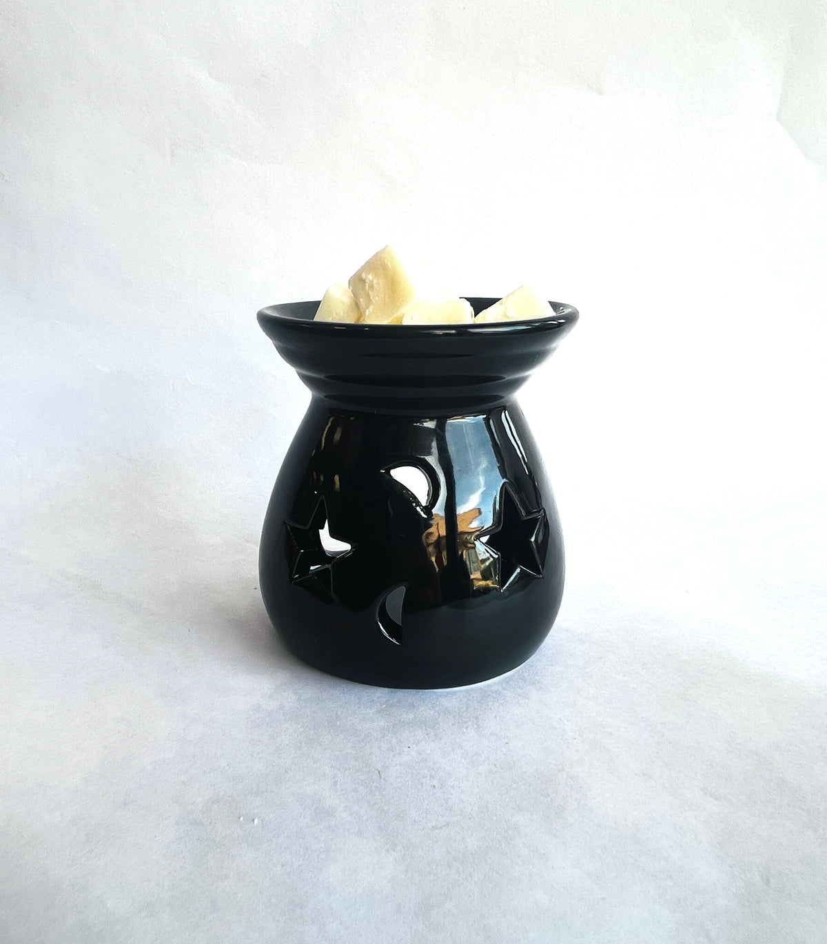 A glossy black wax warmer shaped like a small pot, shown on a light gray background with several pale wax pieces inside the top bowl.