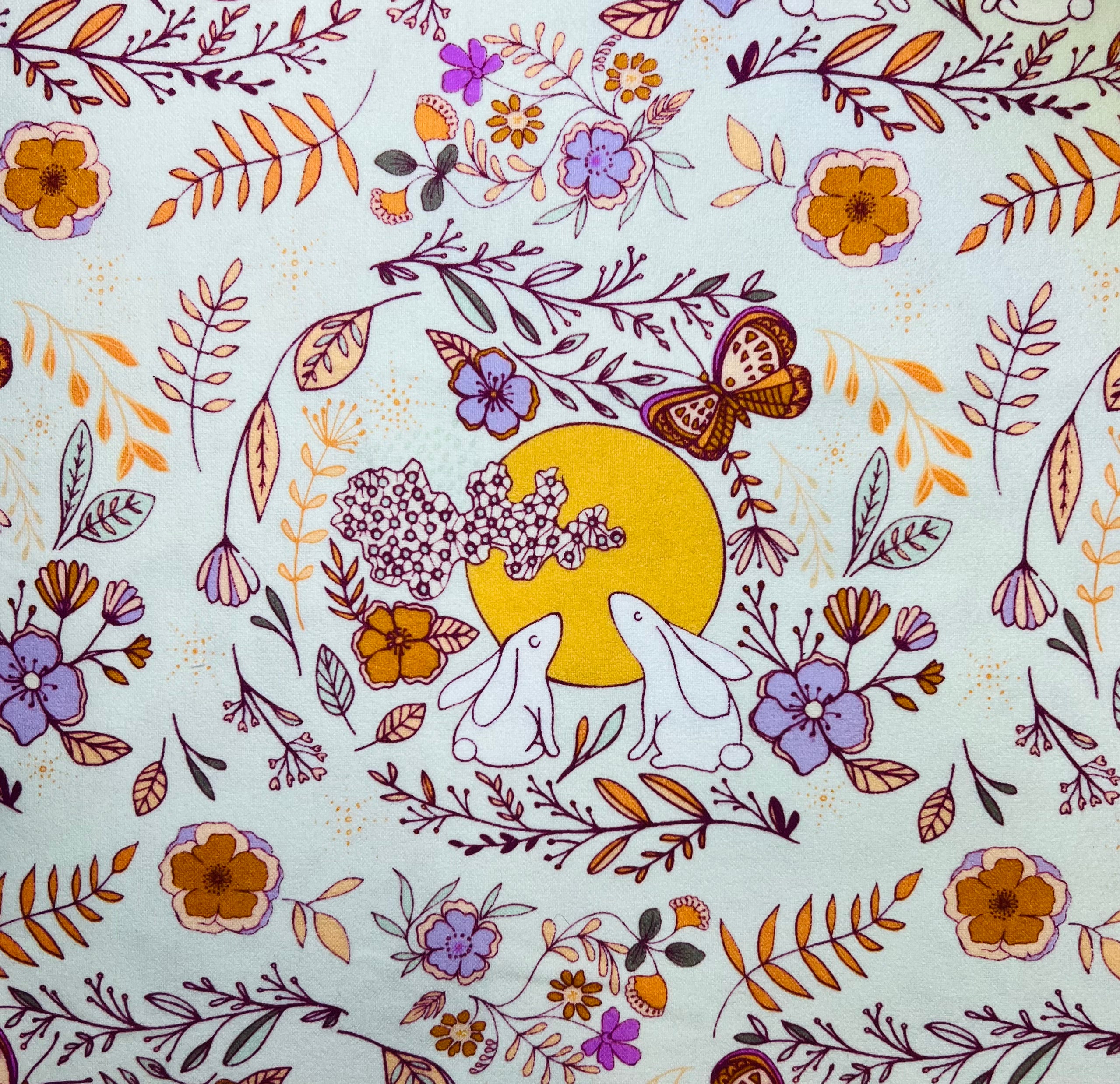Floral pattern with two white rabbits and a yellow circle on a light colored background